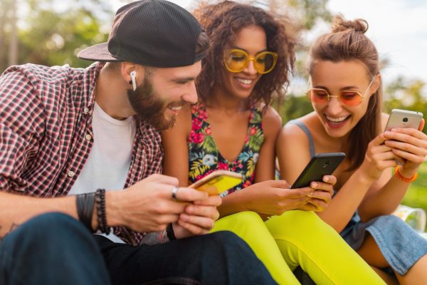 楽しそうに微笑む友人たち、公園で座ってスマートフォンを使う男たち、一緒に楽しむ女たち-1